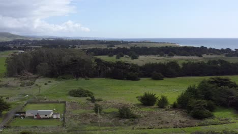 Aerial:-Half-Moon-Bay-beach-and-a-farm-surrounded-by-trees,-flying-forward