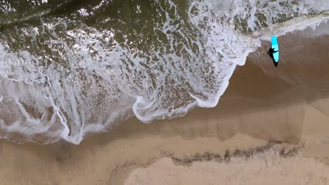 A-top-down-view-of-a-surfer-walking-out-his-surf-board-into-the-ocean-on-a-sunny-day