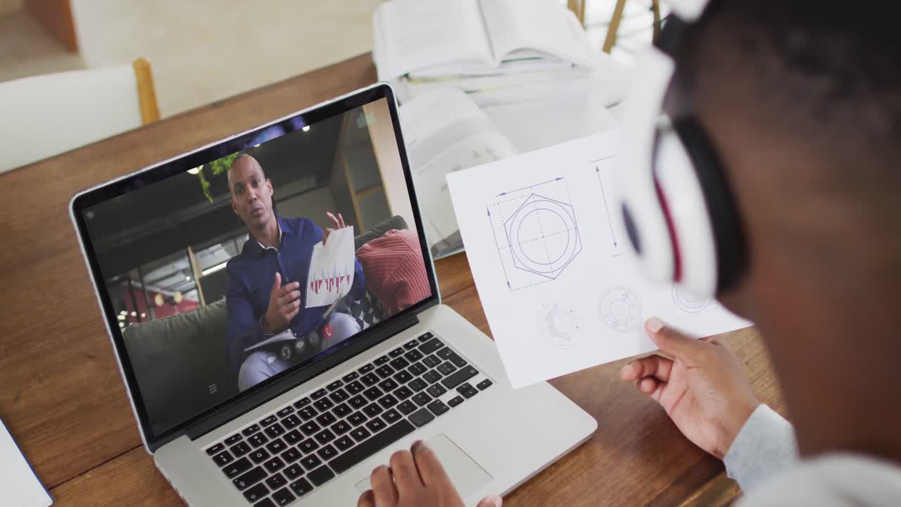 estudiante universitario afroamericano que sostiene notas mientras hace una videollamada en una computadora portátil en casa