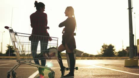 vista trasera de dos atractivas chicas elegantes de pie junto al carrito de compras en el estacionamiento y hablando. una chica en pantalones cortos está de pie