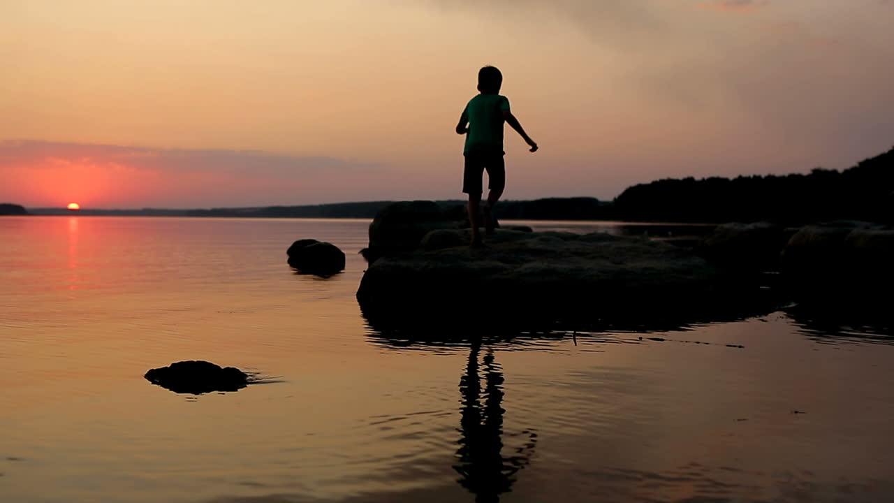 Boy Playing On Stony Beach. Young boy actively playing on stony beach at sunset