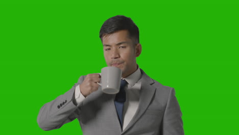 studio shot of businessman in suit holding cup of hot drink against green screen