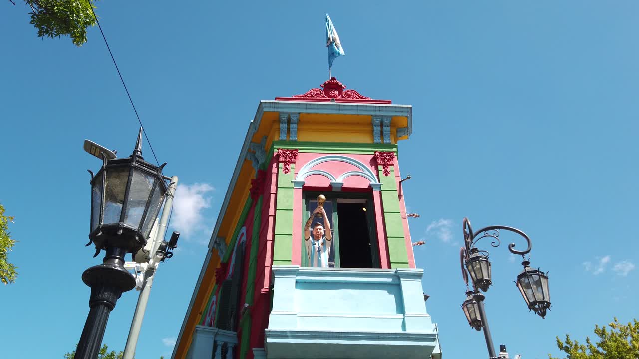 Iconic Lionel Messi statue in colorful houses of Caminito, La Boca, Buenos Aires city, Argentine flag over daylight skyline