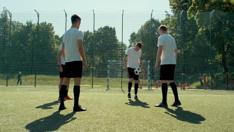 grupo de jóvenes futbolistas entrenando y pasándose el balón entre ellos en un campo de fútbol callejero en un día soleado