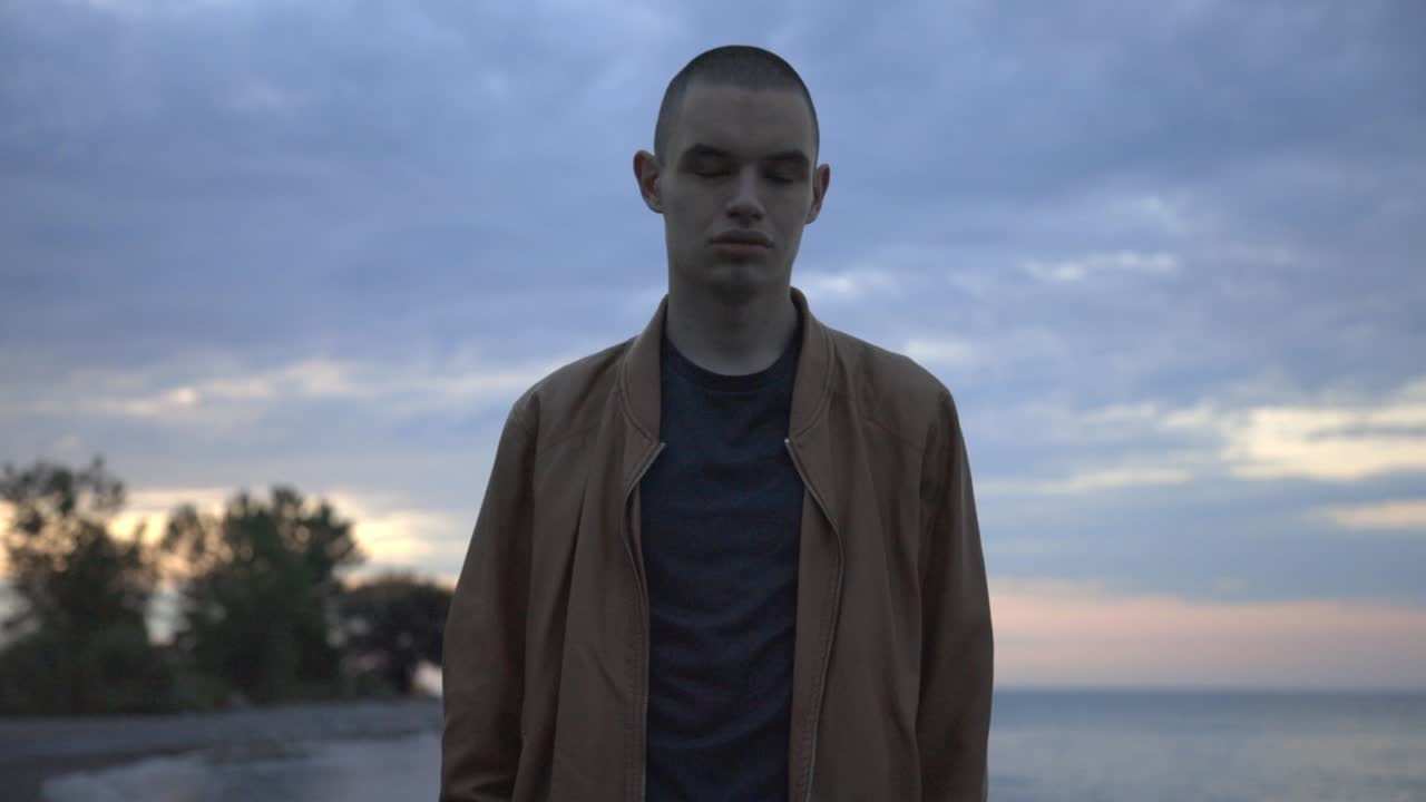 Young Guy Stands By The Shore Suddenly Laughs In Front Of The Camera - Half-Body Shot