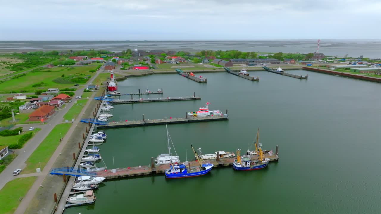 Borkum island harbor with docked vessels, colorful shipyard and wind turbine. Aerial orbit reveals the vast tidal flats of the Wadden Sea, a UNESCO Site