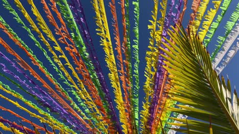 multicoloured ribbons decorating the street in front of the blue sky and palm leaves. 4k