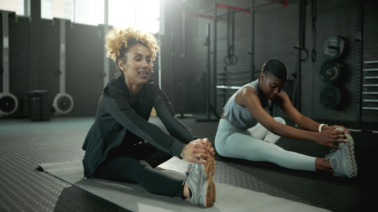 Two women stretching on yoga mats in a gym