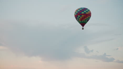 vibrant checkered hot air balloon floating against pastel sky with rhythmic burst of burner flame illuminating wicker basket and distant forest framing serene aerial journey in gentle twilight light