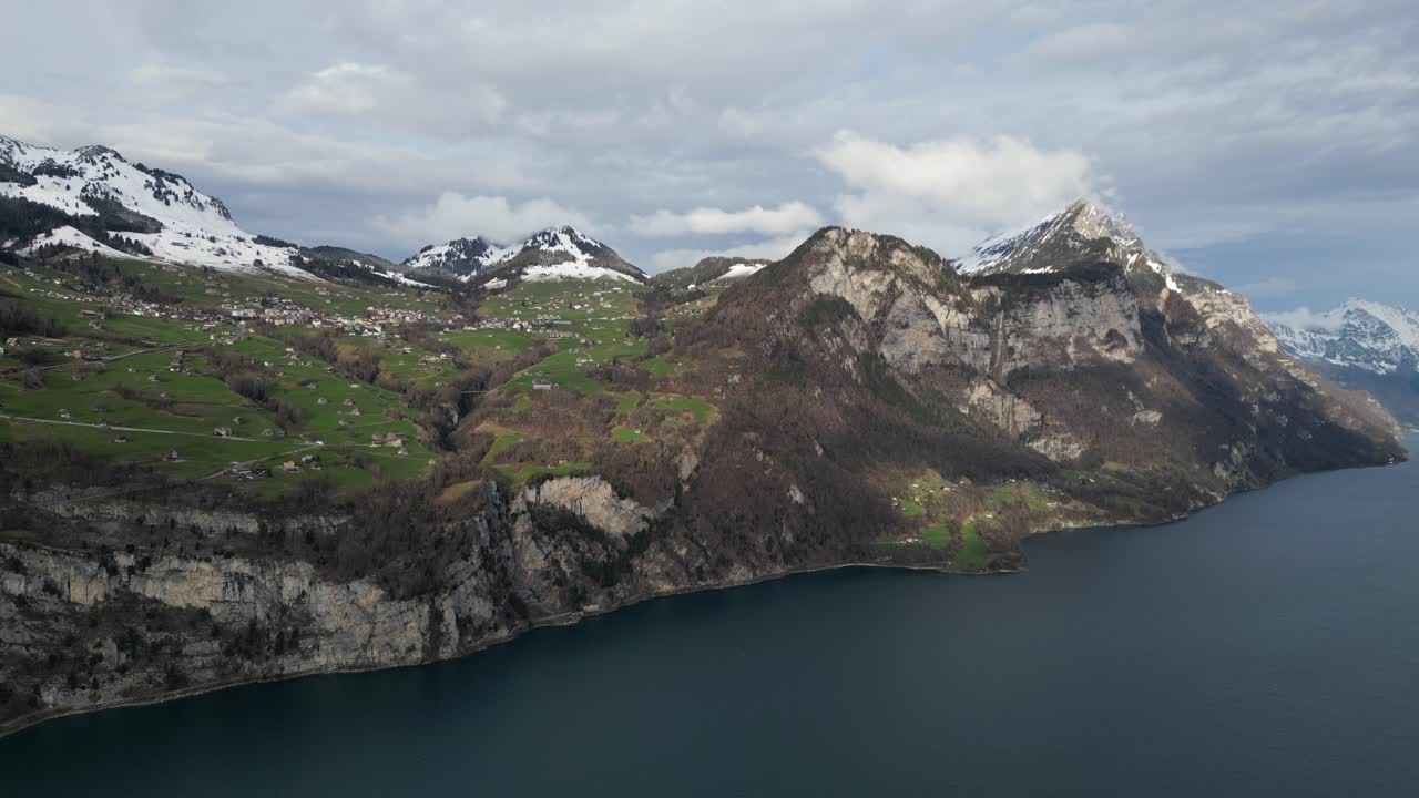 las casas rurales en los prados cubiertos de hierba miran hacia abajo sobre el lago walen en suiza mientras el sol arroja luz y las sombras de las nubes se mueven a través del paisaje.