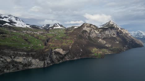 Ländliche-Häuser-In-Grasbewachsenen-Wiesen-Blicken-Auf-Den-Walensee-In-Der-Schweiz,-Während-Die-Sonne-Licht-Wirft-Und-Wolkenschatten-über-Die-Landschaft-Ziehen