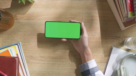 vista de arriba hacia abajo de una computadora portátil con pantalla verde simulada pantalla chromakey en un escritorio de oficina de madera al lado de la libreta con bolígrafos, gafas y un vaso de agua.