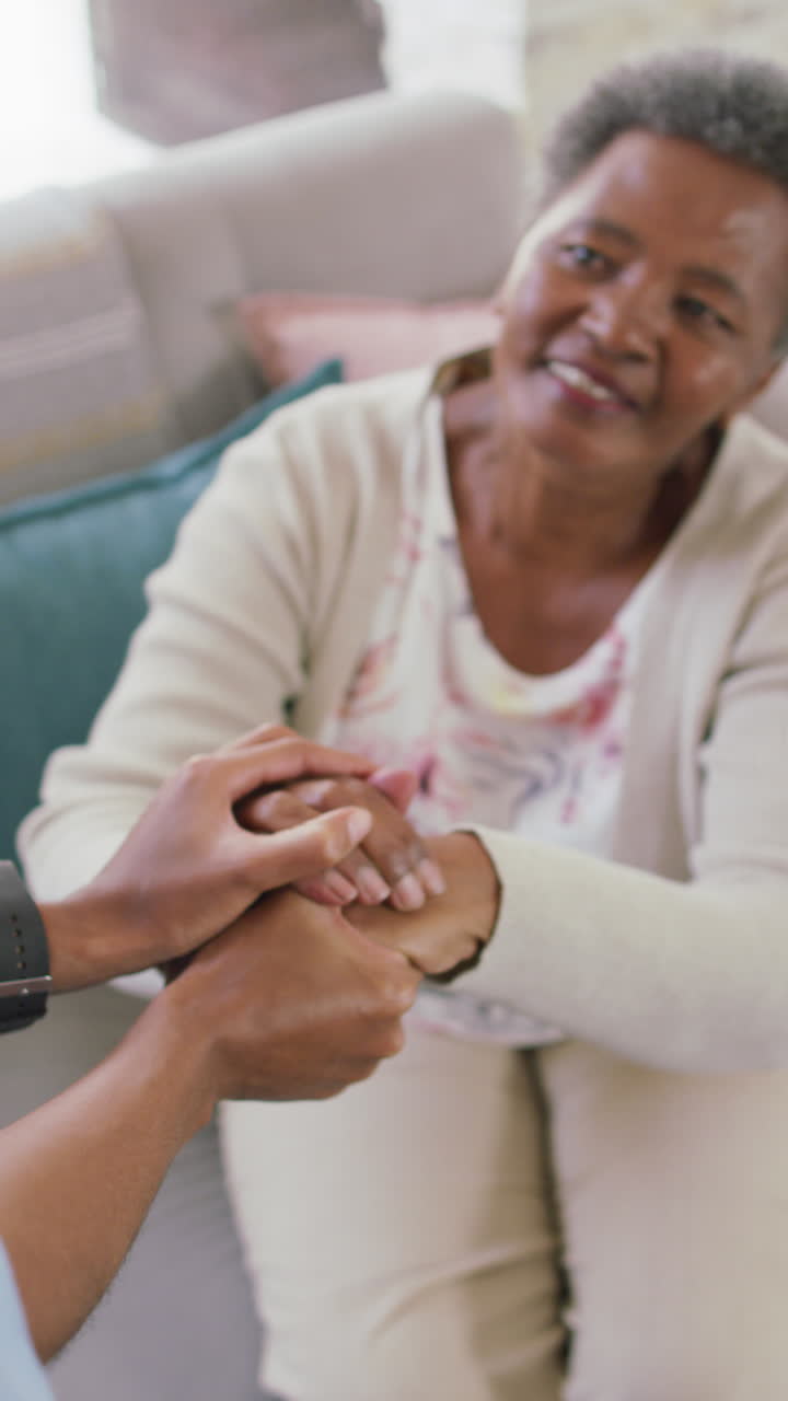 video vertical de una mujer afroamericana mayor sosteniendo la mano de una fisioterapeuta femenina en casa
