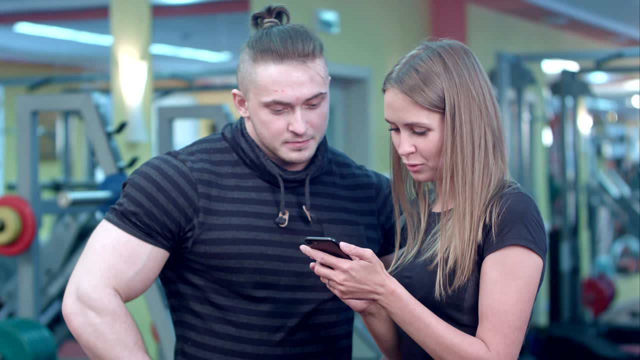 joven en el gimnasio añadiendo el número de su instructor de fitness a la lista de contactos telefónicos