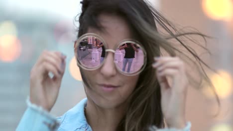 una mujer joven posando con grandes gafas de sol redondas y divertidas, el viento soplando el cabello