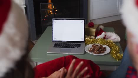 Back-view-of-caucasian-couple-wearing-santa-hats-using-laptop-with-copy-space-on-screen