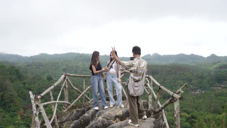 young asian indonesian friends taking photo on mountain viewpoint with phone, nature travel