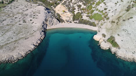 aerial view of a barren mediterranean coast with a beach and the crystal clear sea water where you can look deep through the water