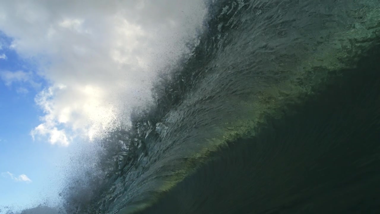 Dark green ocean wave rising under overcast clouds and spray in detailed slow motion