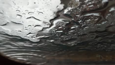 vista abstracta en cámara lenta de las gotas de lluvia aterrizando en el vidrio como se ve desde abajo, debajo, cielo gris