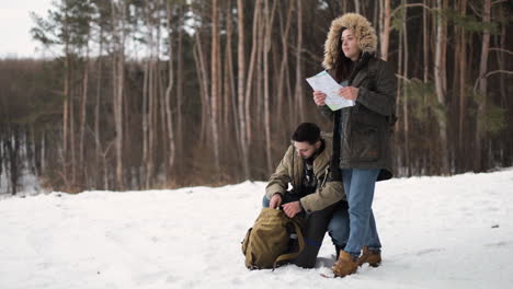 pareja caucásica revisando el mapa para obtener direcciones en un bosque nevado.