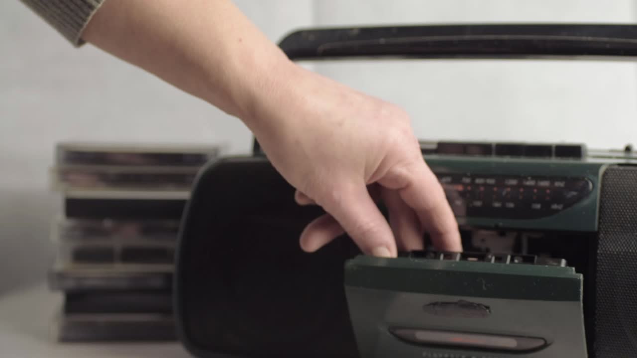 Hand ejecting retro cassette tapes into radio cassette player wide shot