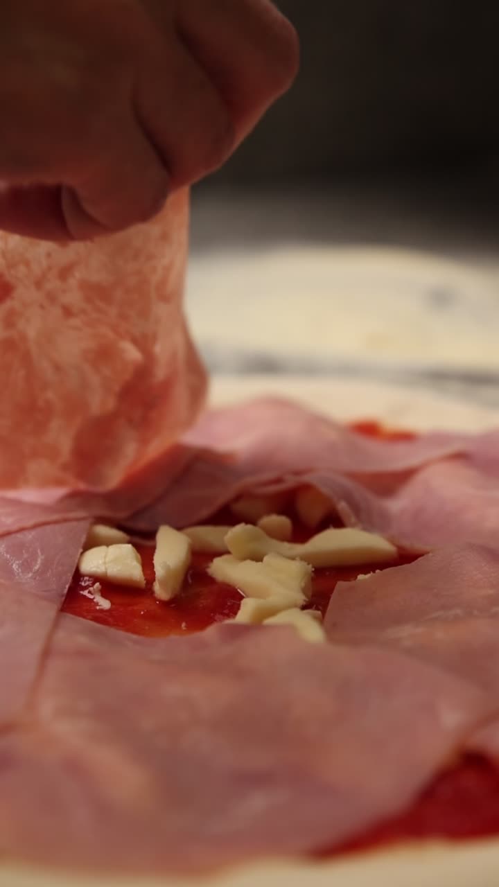 Mano che adagia fette di prosciutto sull'impasto della pizza con formaggio