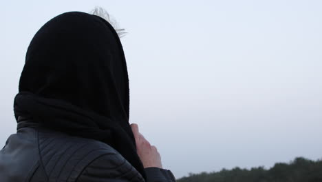 Back-shot-over-the-shoulder-of-a-cold-person,-male-or-female,-standing-in-nature-with-a-scarf-wrapped-around-head