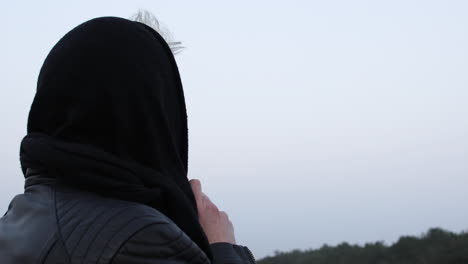 back shot over the shoulder of a cold person, male or female, standing in nature with a scarf wrapped around head