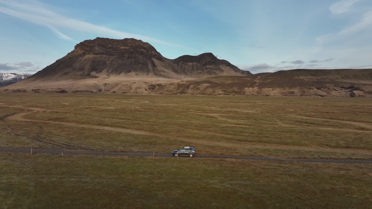 아이슬란드 부르펠 (búrfell) 의 외 도로를 따라 운전하는 suv의 공중 촬영, 배경에는 넓은 잔디 평야와 거친 산이 있습니다.