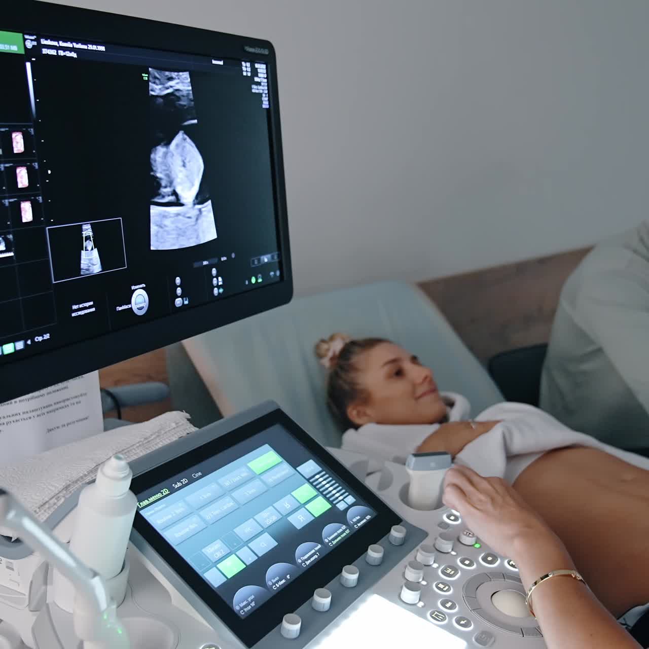 Hamile bir kadının sonografi muayenesi. Doktor, makine düğmelerine basarak ekipmanın başında oturuyor.