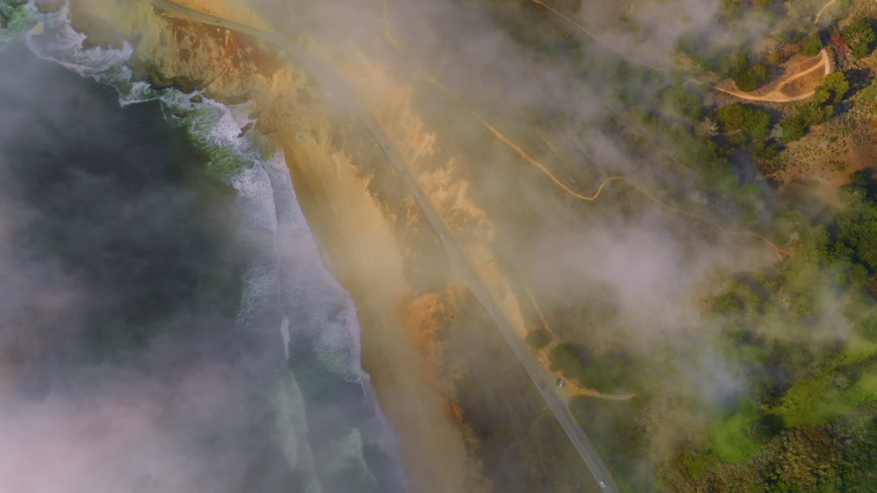 Rocky beach with waves coming back and forth. Highway with cars moving by in the mountains. Amazing scenery covered with fog in Montara, California, USA.