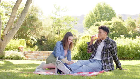 Happy-diverse-couple-having-picnic-in-sunny-garden,-in-slow-motion