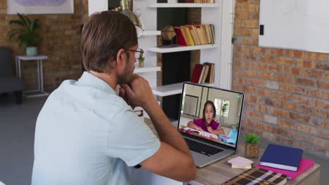 caucasian male teacher sitting at desk using laptop having online school lesson