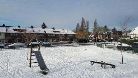 Dolly-in-of-slide-and-seesaw-in-a-snow-covered-children's-play-park-in-a-suburban-neighborhood