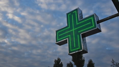 illuminated green pharmacy cross in front of the drugstore