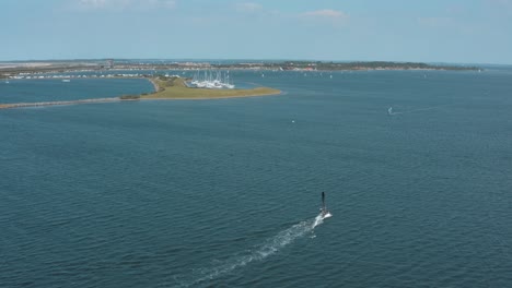 Drone---Aerial-shot-of-surfer-on-a-blue,-wavy-and-windy-sea-on-a-sunny-day-with-white-clouds-on-a-island,-30p