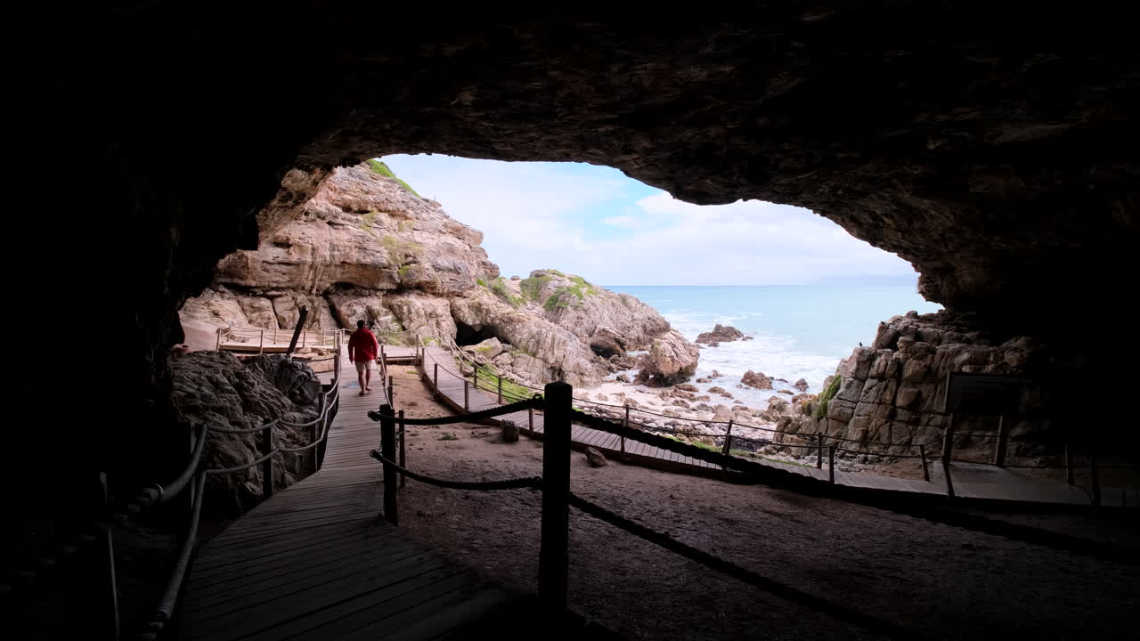 View from inside Klipgat Cave of male tourist on wooden boardwalk, De Kelders