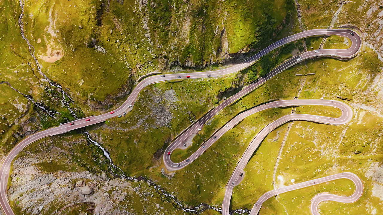 Cars move by the wavy road on the mountain slope. Drone footage above the Transfagarash highway in the Carpathian Mountains, Romania