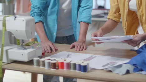 close up of male and female designers' hands with sewing machine rearranging clothes drawing picture while designing clothes in the studio