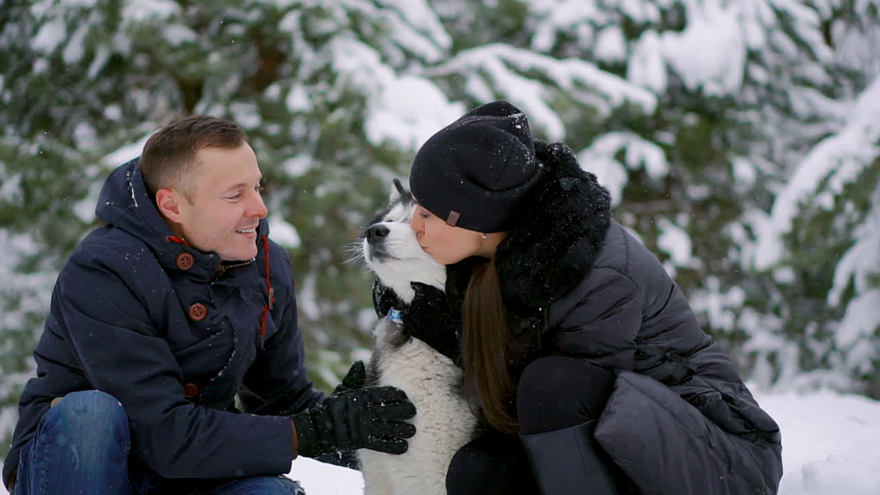 아름다운 가족, 남자와 개와 함께 겨울 숲에 있는 여자. 개 시베리안 허스키와 놀아보세요.