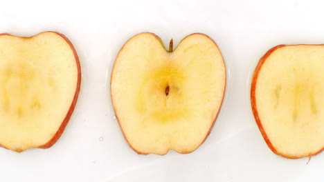 movimiento lento de una salpicadura de agua en tres rebanadas de una manzana roja que se encuentra en un fondo blanco en el agua