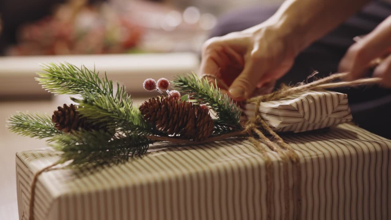 Hands Tie Twine Around a Christmas Gift, Decorated With Pine Sprigs and Pinecones - Close Up