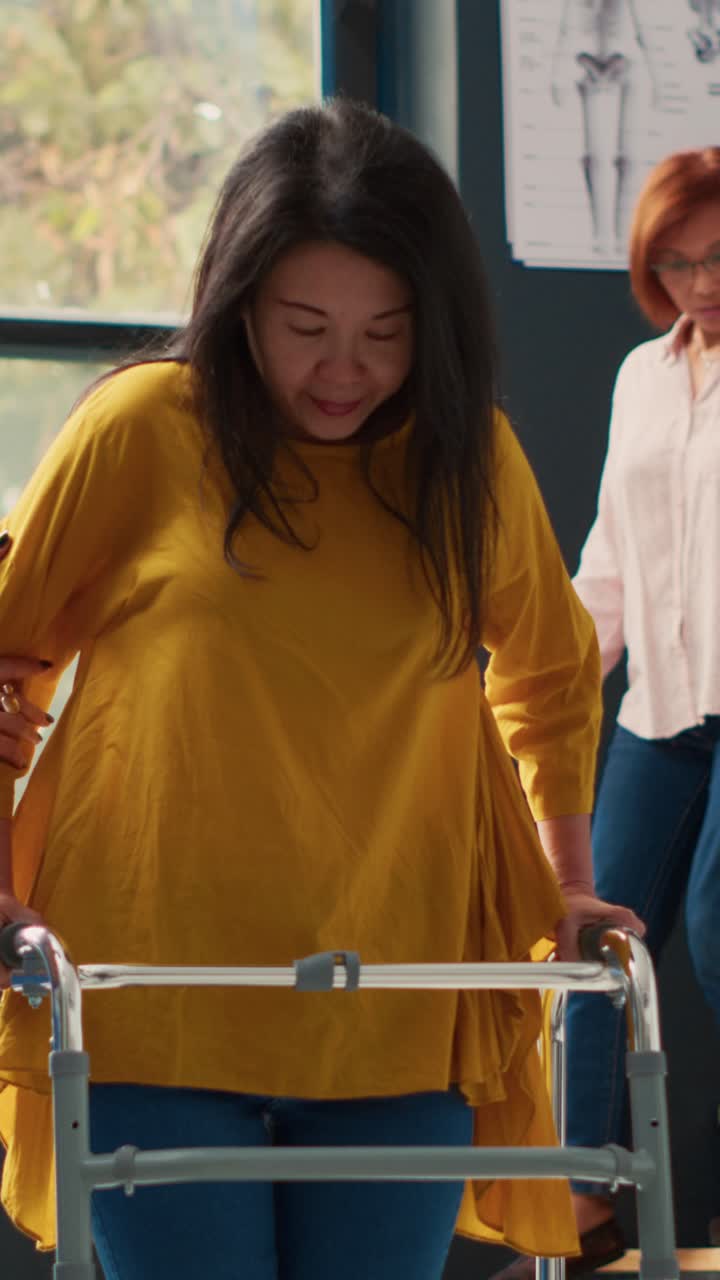 Vertical video: Nurse helping asian woman to walk with walking frame