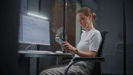 female stock exchange trader monitoring real-time stocks, exchange market charts on digital tablet and computer with multi-monitor desktop. investment agent working in office at night. vertical shot.