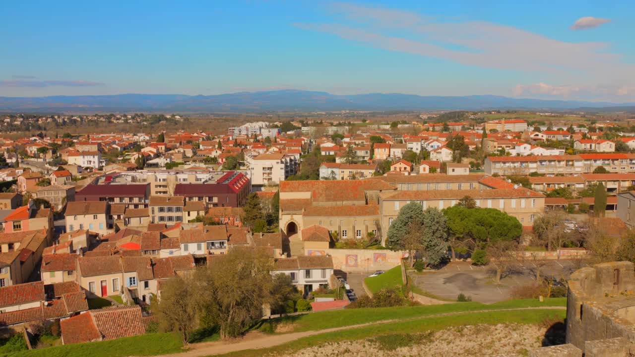 Scenic view of Carcassonne, France, showing a cityscape with rooftops, mountains, and blue skies