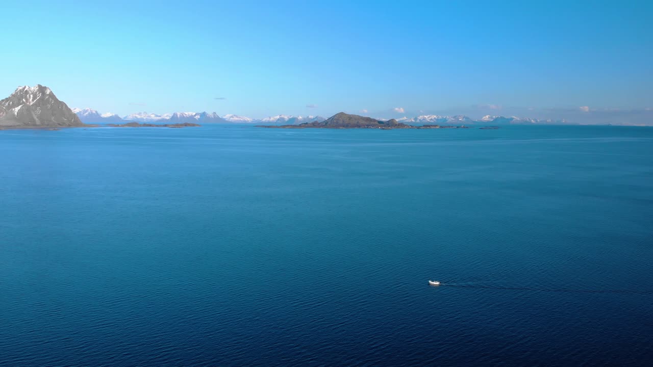 Aerial drone shot of the blue ocean in Lofoten, Norway and mountains in the background.