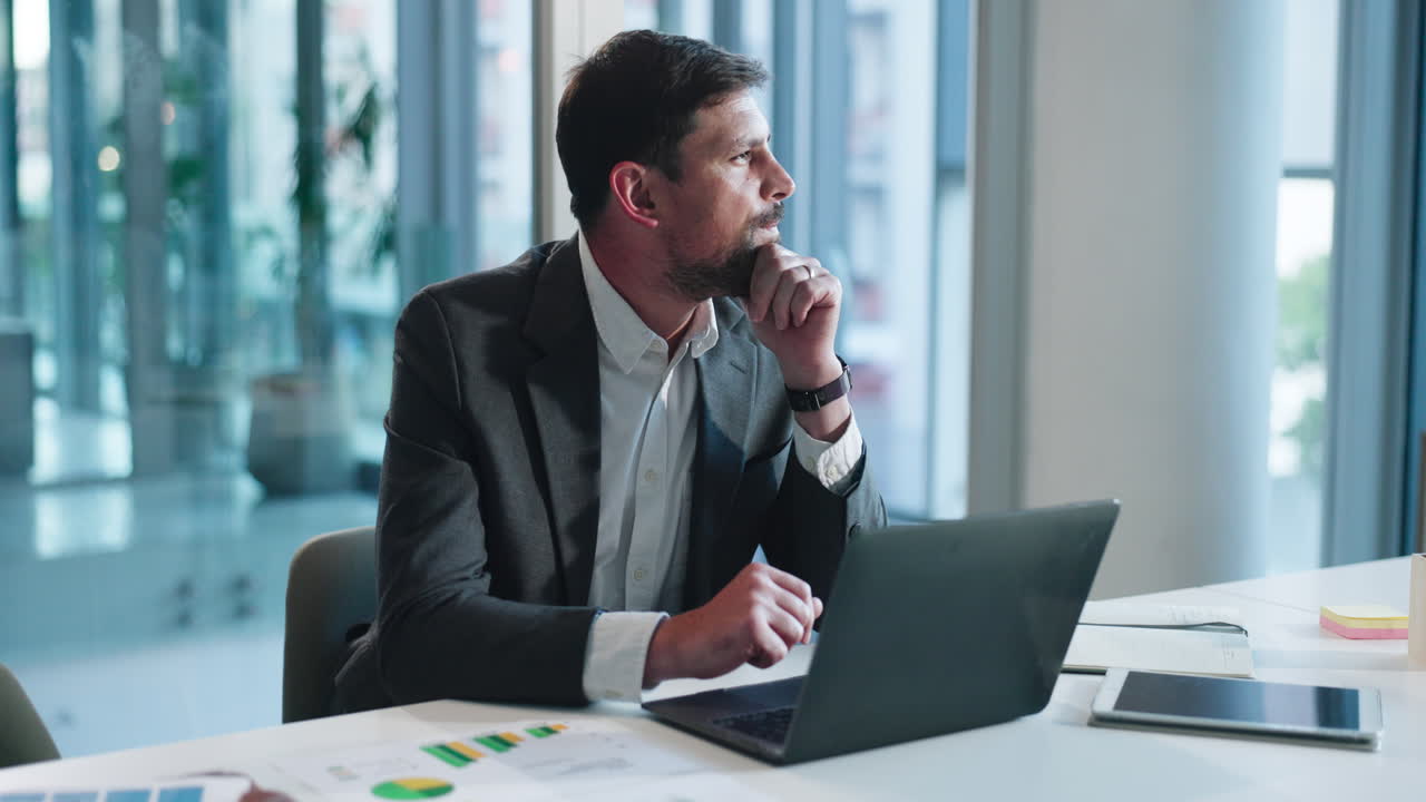 Uomo d'affari pensieroso che lavora al laptop in un ufficio moderno