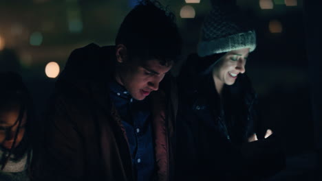 group of friends relaxing on rooftop at night using smartphone technology browsing social media chatting online enjoying weekend gathering