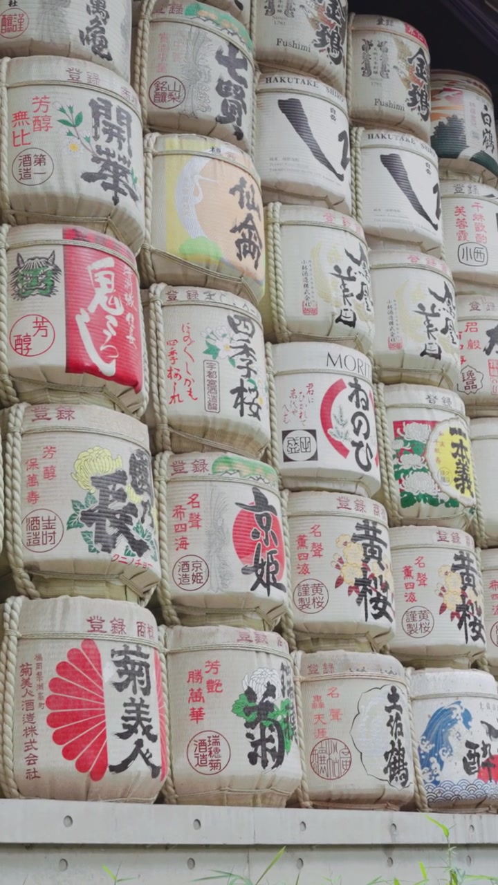 Vertical wide slow-motion video of colorful and beautiful sake barrels at Meiji Jingu Shrine during the daytime in Yoyogi Park in Tokyo.